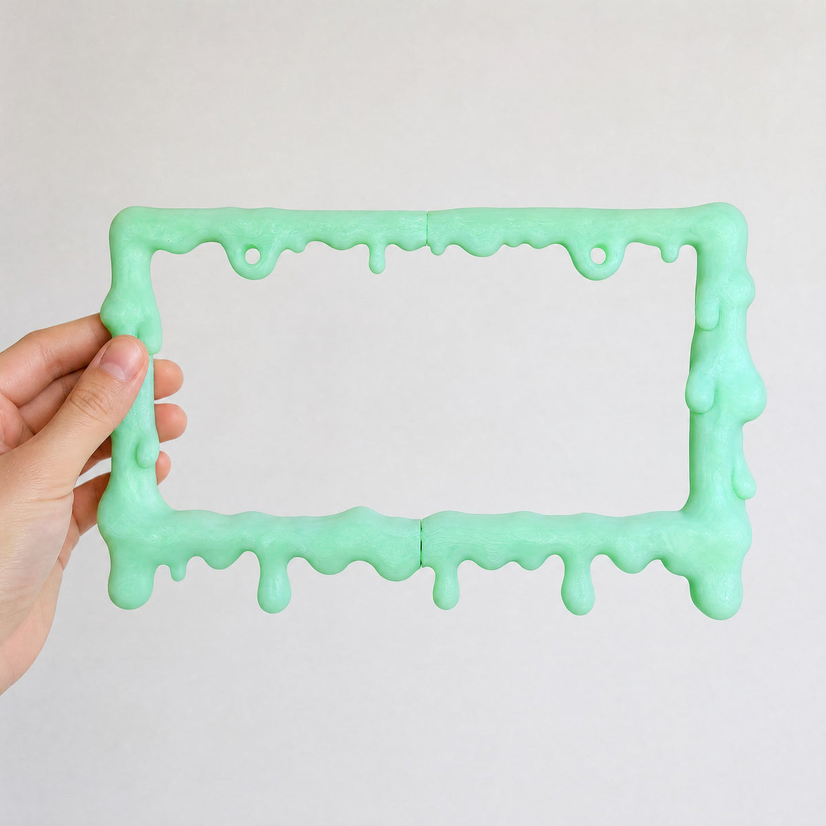 Glow green slime license plate frame on a warm grey backdrop