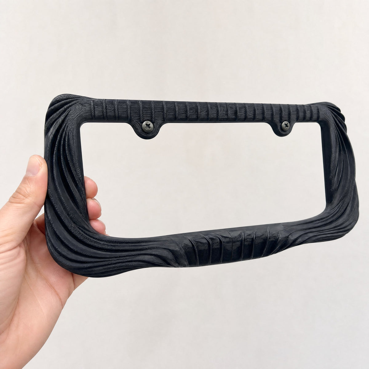 Black Utopia license plate frame held in a hand to show its size